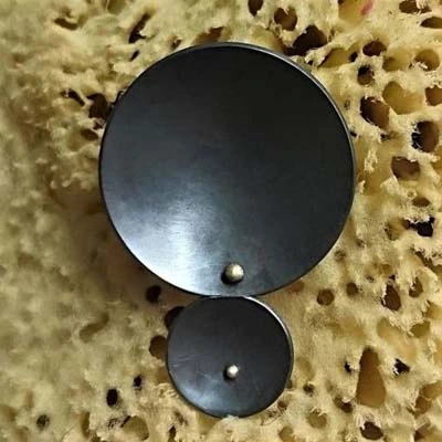 Pendentif rond pâtiné noir par granulation en laiton présenté sur un fond