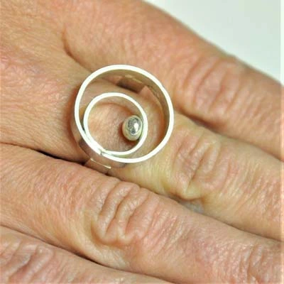 Bague volumineuse design croisé en ruban argent portée au doigt